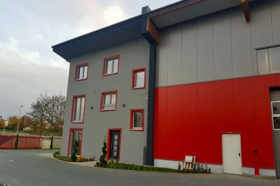 Moderne Gebäude mit grauer und roter Fassade, großen Fenstern und einem Eingang.